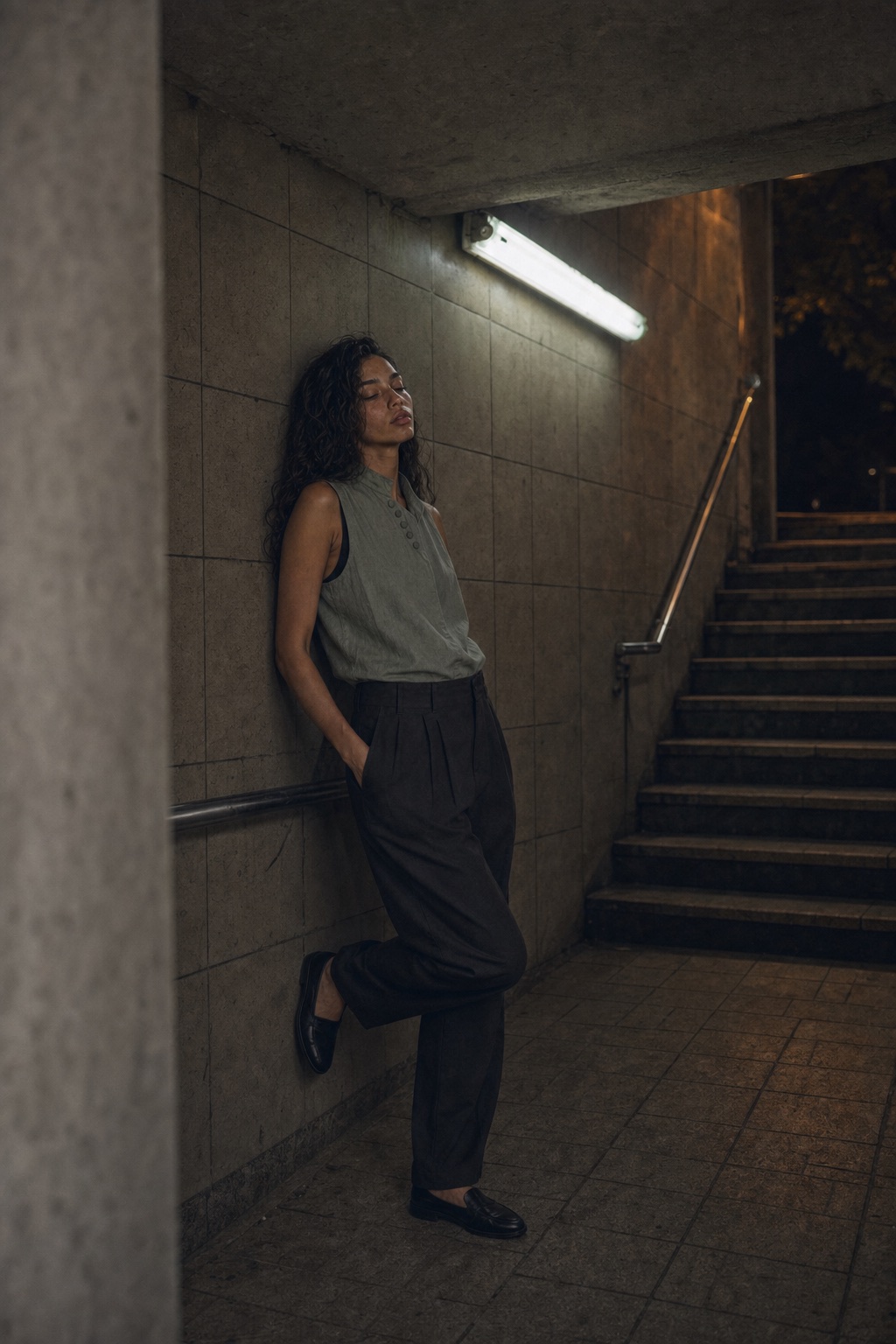 Leandra leaning under station light in mineral wool and dark trousers